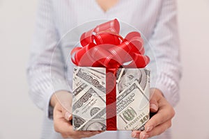 Woman holding gift box wrapped in dollars on background, closeup