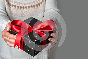 Woman holding gift in her hands. Red bow. Gray background. Christmas or Valentine's Day