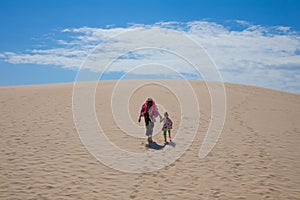 Woman holding girl hand walking up the dune of Bolonia Beach in photo