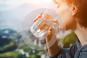 Woman holding glass of crystal clear natural water, drinking, nature mountain background