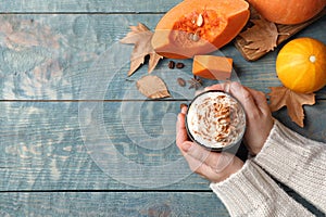 Woman holding glass cup of tasty pumpkin spice latte on wooden table