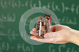 Woman holding glass jar of coins and graduation cap against greenboard, closeup with space for text. Scholarship concept
