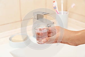 Woman holding glass with mouthwash for teeth and oral care