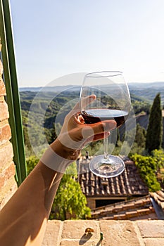 Woman holding a glass of red wine with beautiful landscape of Italy in a background on a sunny day.