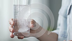 Woman holding glass of water, putting tablet of aspirin into it, painkiller