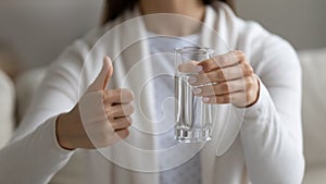 Woman holding glass of water showing thumbs up closeup view