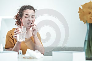 Woman holding glass of water while taking allergy medication