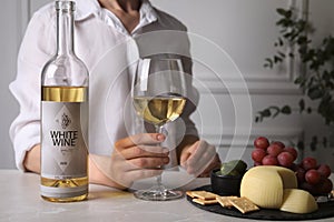 Woman holding glass of white wine at table with snacks, closeup