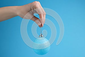 Woman holding glitter Christmas ball on light blue background, closeup. Space for text