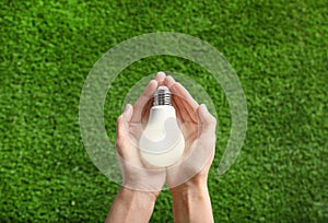 Woman holding glowing light bulb over green grass, top view