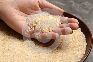 Woman holding grains near plate with parboiled rice on table