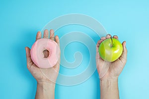 Woman holding green apple and pink donut, female choose between fruit is Healthy food and sweet is unhealthy junk foods. Dieting,