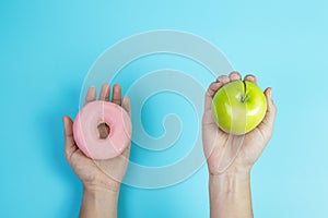 Woman holding green apple and pink donut, female choose between fruit is Healthy food and sweet is unhealthy junk foods. Dieting,