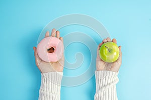 Woman holding green apple and pink donut, female choose between fruit is Healthy food and sweet is unhealthy junk foods. Dieting,