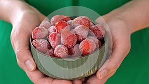 Woman holding green bowl full of frozen strawberries in her hands.