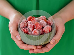 Woman holding green bowl full of frozen strawberries in her hands