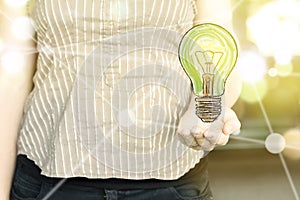 Woman holding a green light bulb with as `green thinking` concept on a sunny day