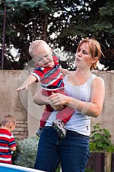 Woman holding grumpy crying toddler boy outdoors