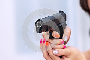 Woman holding gun in hand at home. Focus hand of young women using black gun protection from danger gesture killer