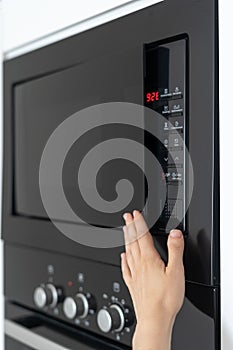 Woman holding hand on black microwave door