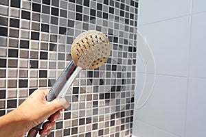 Woman holding in hand corroded limescale calcified old shower head hanging from a stand inside cabin
