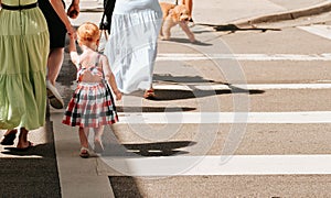Woman holding the hand of a little girl in a beautiful dress while crossing the street