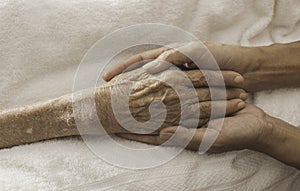 A woman holding a hand An old woman lying in bed sick