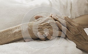 A woman holding a hand An old woman lying in bed sick