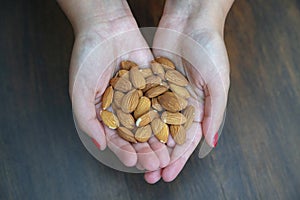 Woman holding a handful of almonds, the edible seeds of Prunus dulcis, ideal serving size of nuts for a healthy natural snack