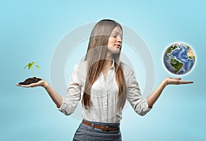 Woman holding handful of soil with plant in one hand and globe in the other