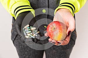 A woman holding in hands an apple and capsules with vitamins.