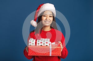 Woman holding in hands christmas gifts in santa claus hat on blue background Xmas concept