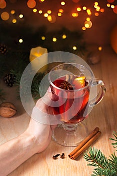 Woman holding in hands glass of aromatic mulled wine Christmas tree with lights. Festive atmosphere, cozy winter mood