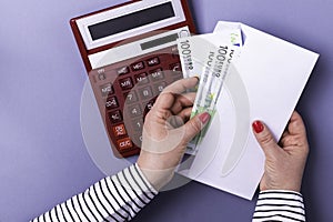 Woman holding hands holding an envelope with cash on the background of a calculator on a blue background. Euro banknotes.