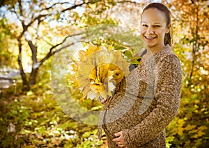 Woman holding hands with maple leaves on her pregnant belly