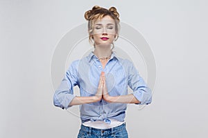 Woman holding hands in namaste or prayer, keeping eyes closed while practising yoga and meditating at home alone, having calm loo