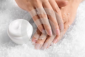 Woman holding hands near jar of cream on decorative snow.