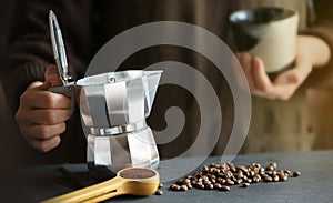 Woman holding in hands traditional moka pot coffee maker ready to pouring fresh coffee inside to the small cup. Coffee