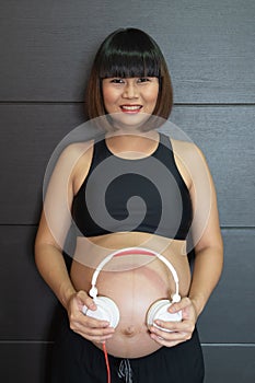 Woman holding headphone on her big belly happiness
