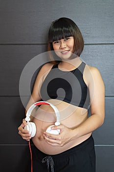 Woman holding headphone on her big belly happiness