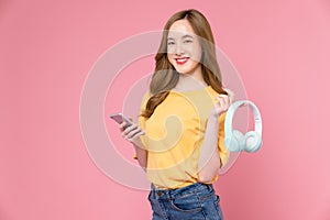 woman holding headphones listening to music and enjoy favourite playlist application on smartphone with dancing on pink background