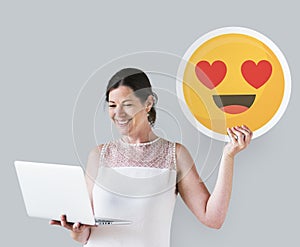 Woman holding a heart eyes emoticon and a laptop