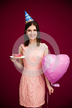 Woman holding heart shaped balloon and donut with candle