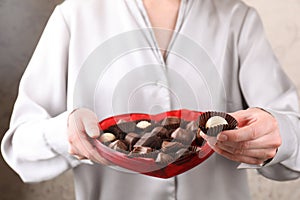 Woman holding heart shaped box with delicious chocolate candies, closeup