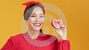 Woman holding heart-shaped box on the orange background.