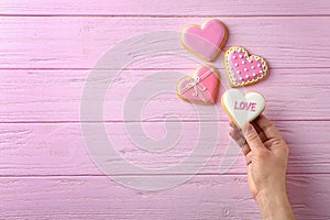 Woman holding heart shaped cookie with word Love on wooden background, top view.