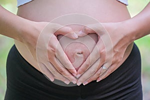 Woman holding her hands in heart shape on her pregnant belly