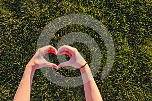 Woman holding her hands in a heart shape symbol near the fresh green grass, love nature