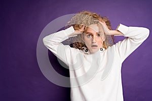 woman holding her head with two hands ruining her hair in a white sweater on a purple background