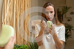 Woman holding her long hair, looking at damaged split ends, problems with hair care